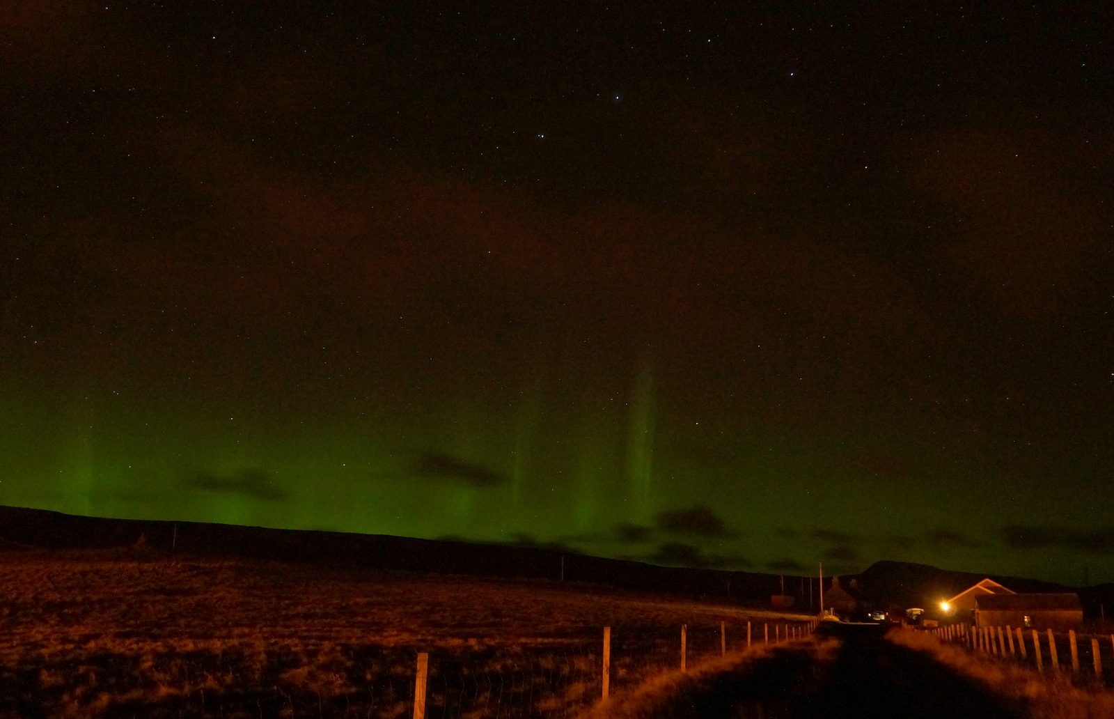 Green northern lights low over a road at Baltasound in Shetland