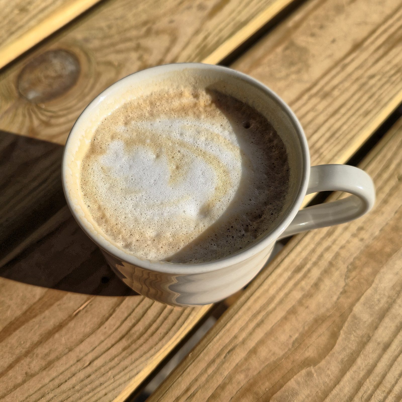 A flat white coffee in a mug on a wooden cafe table, seen from above