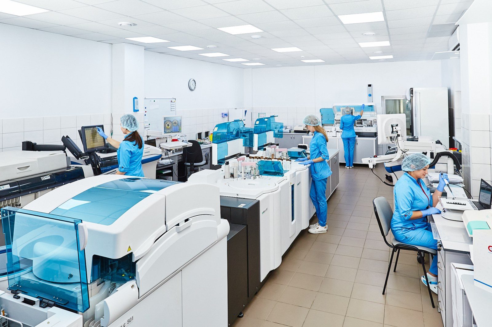 Scientists in blue scrubs working at automated analysers in a modern laboratory