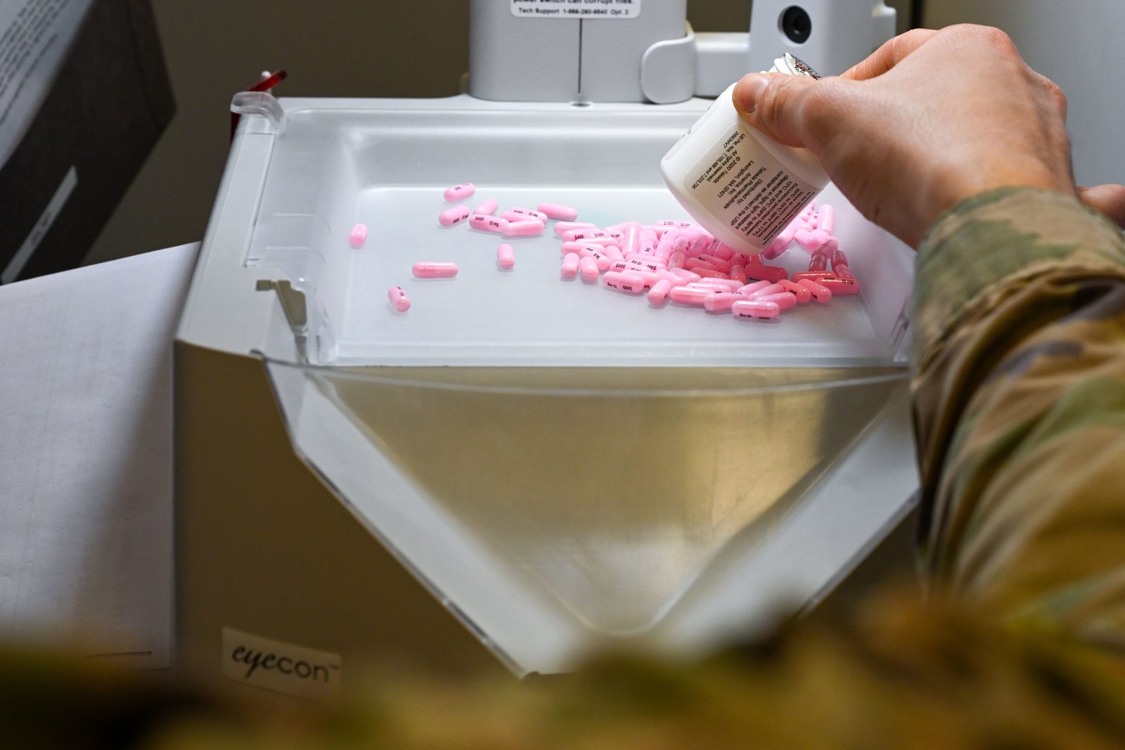 A hand pouring pink pills from a bottle onto the tray of an automated pill counter in a pharmacy
