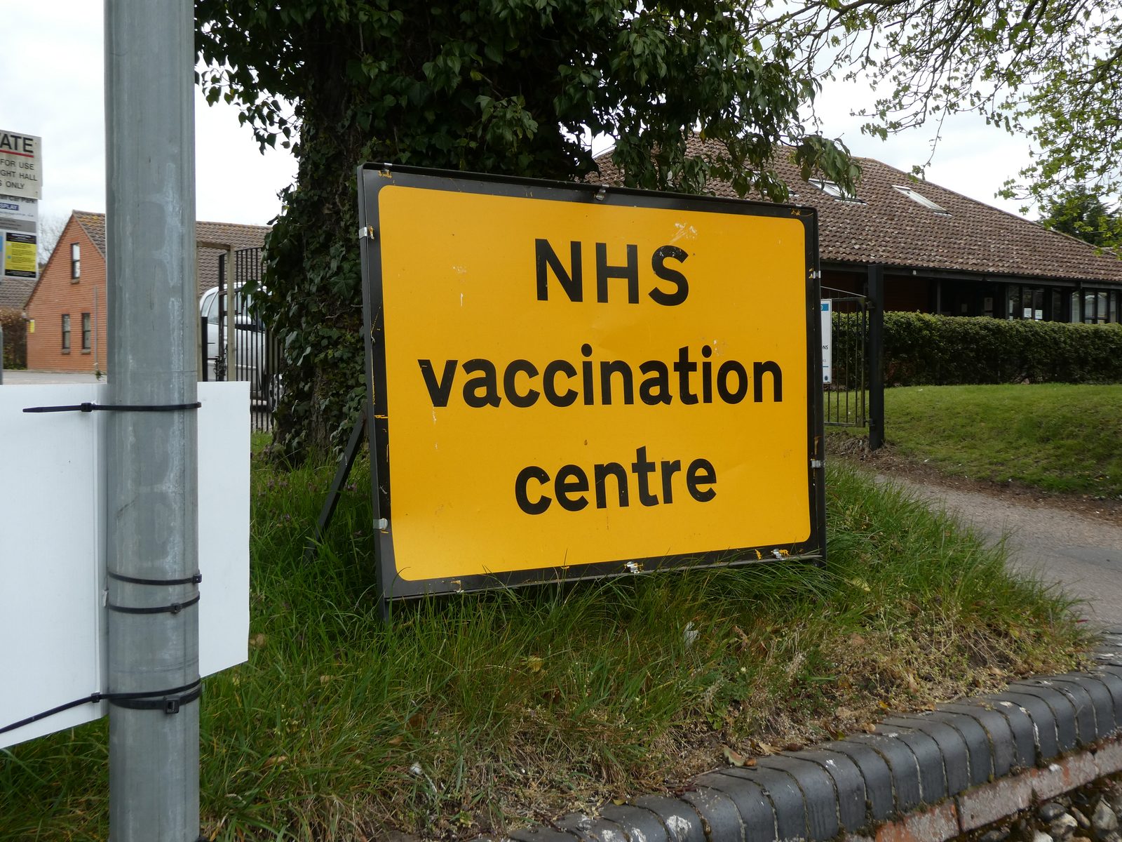 A yellow sign reading NHS vaccination centre on a grass verge