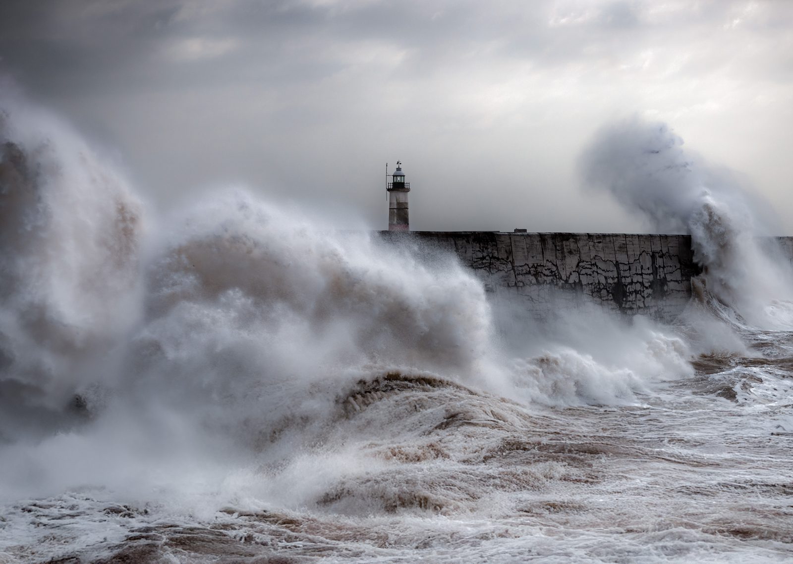 Huge waves crashing over the harbour wall and lighthouse at Newhaven in East Sussex during a storm