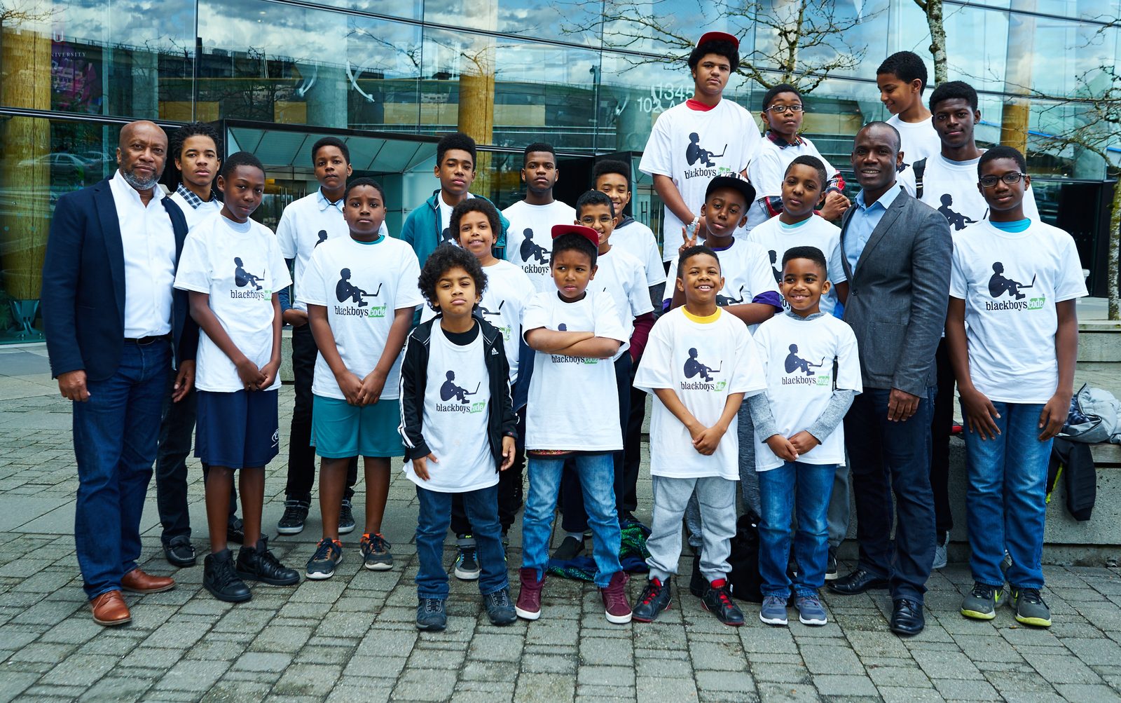 Young participants in a coding programme posing in their programme T-shirts outside a technology building