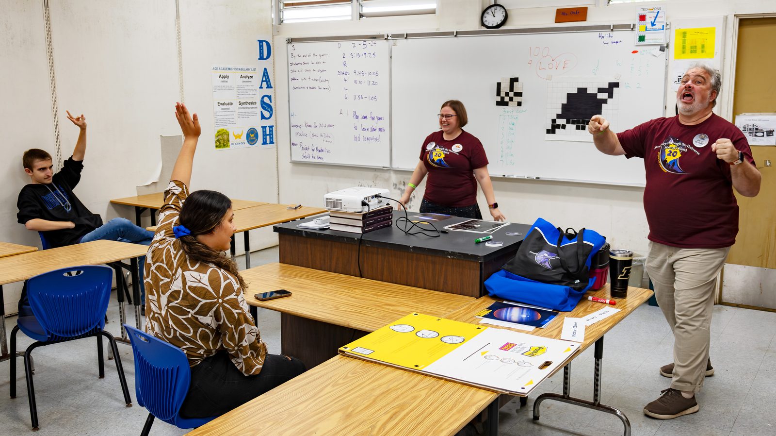 Students raising their hands during a computer science demonstration in a classroom