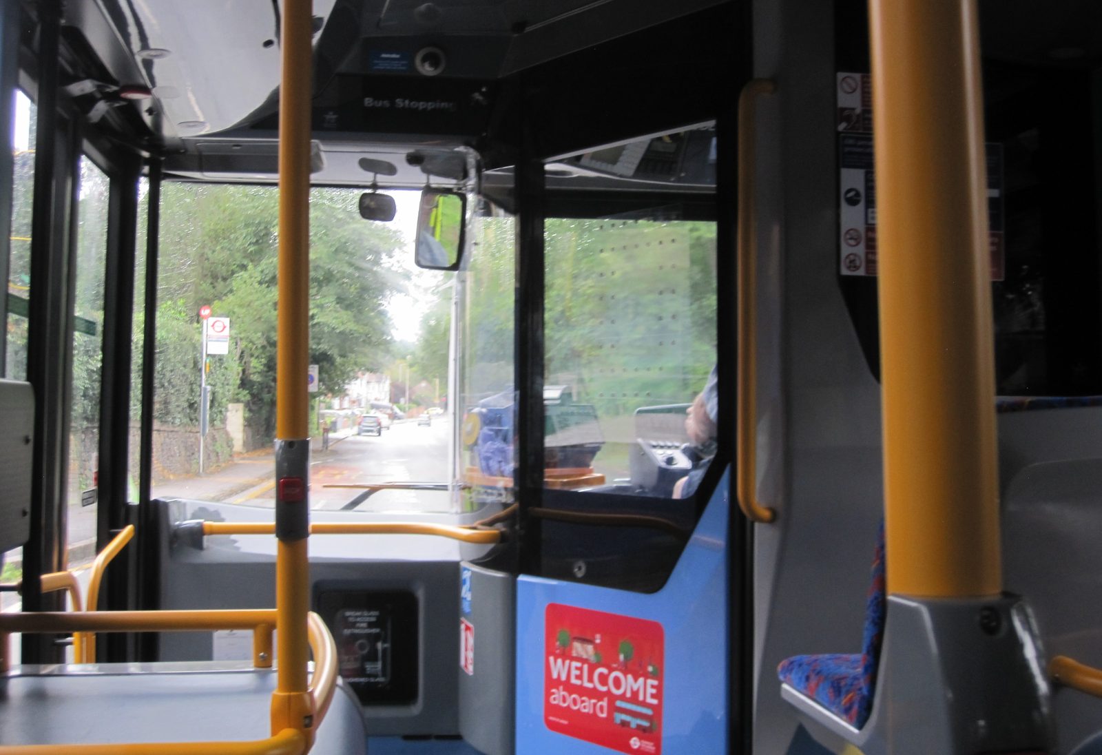 The view towards the cab inside a London bus on route 427, with yellow handrails and a Welcome aboard sign