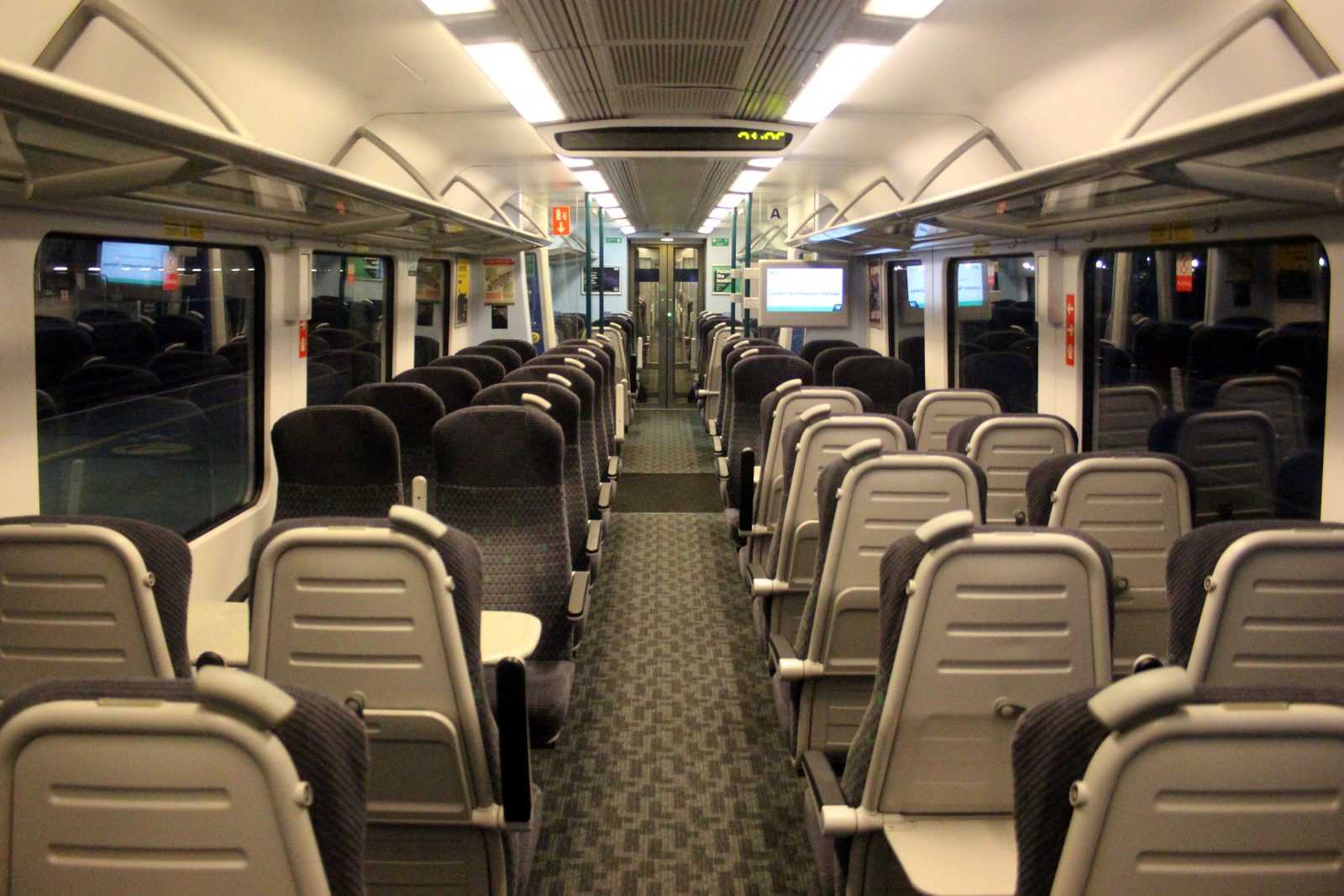The empty refurbished standard class interior of a West Midlands Trains Class 350, with rows of blue seats and tables