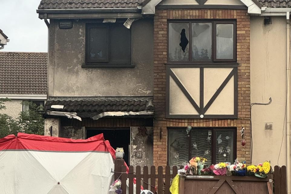 The fire-damaged family home in Birchwood, Waterford, with floral tributes at the front fence